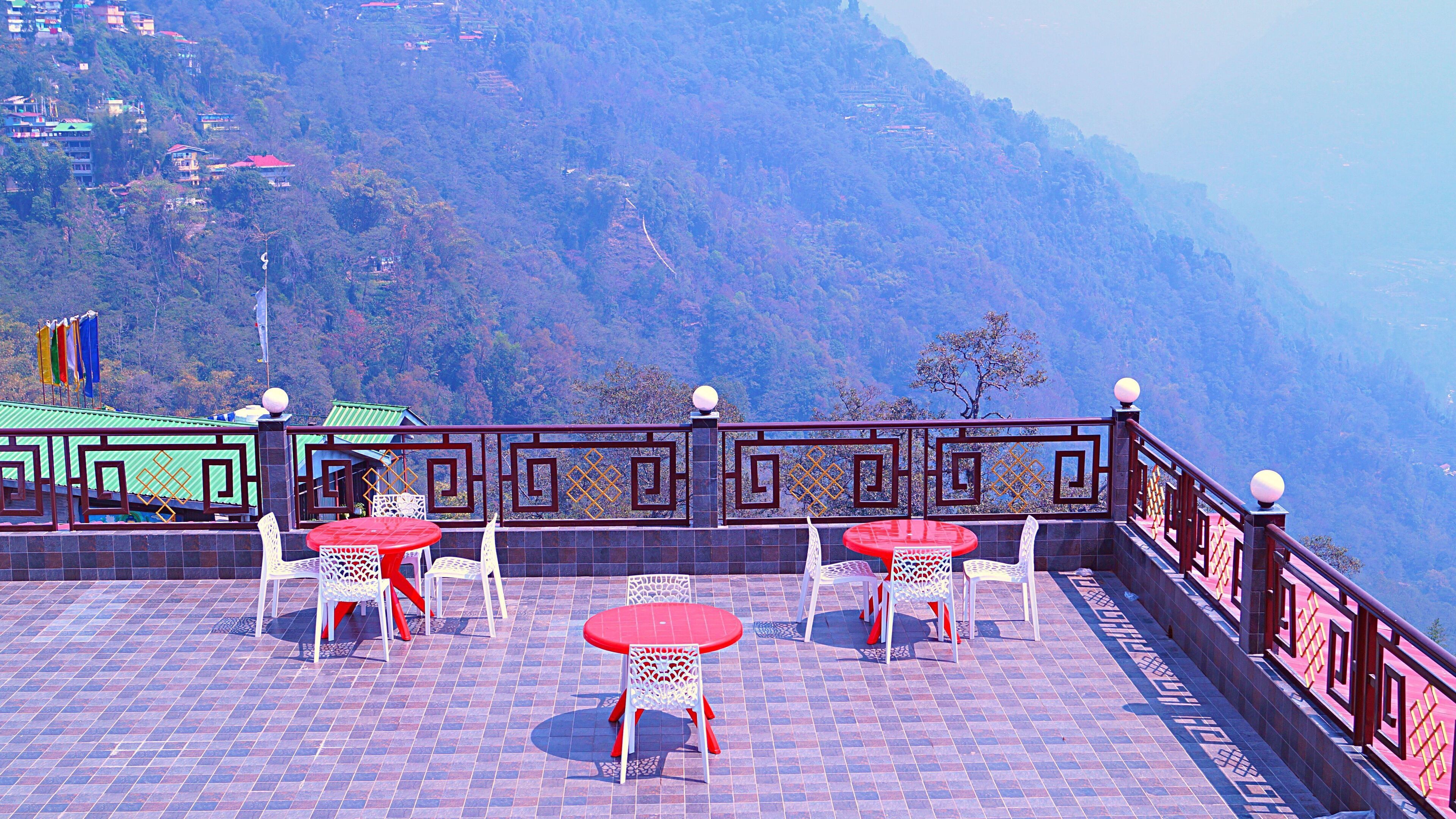 A terrace with red tables and white chairs, overlooking a mountainous landscape.