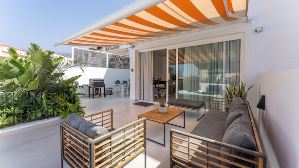 Un'area esterna moderna con patio, zona salotto e una parte coperta con tenda a righe.