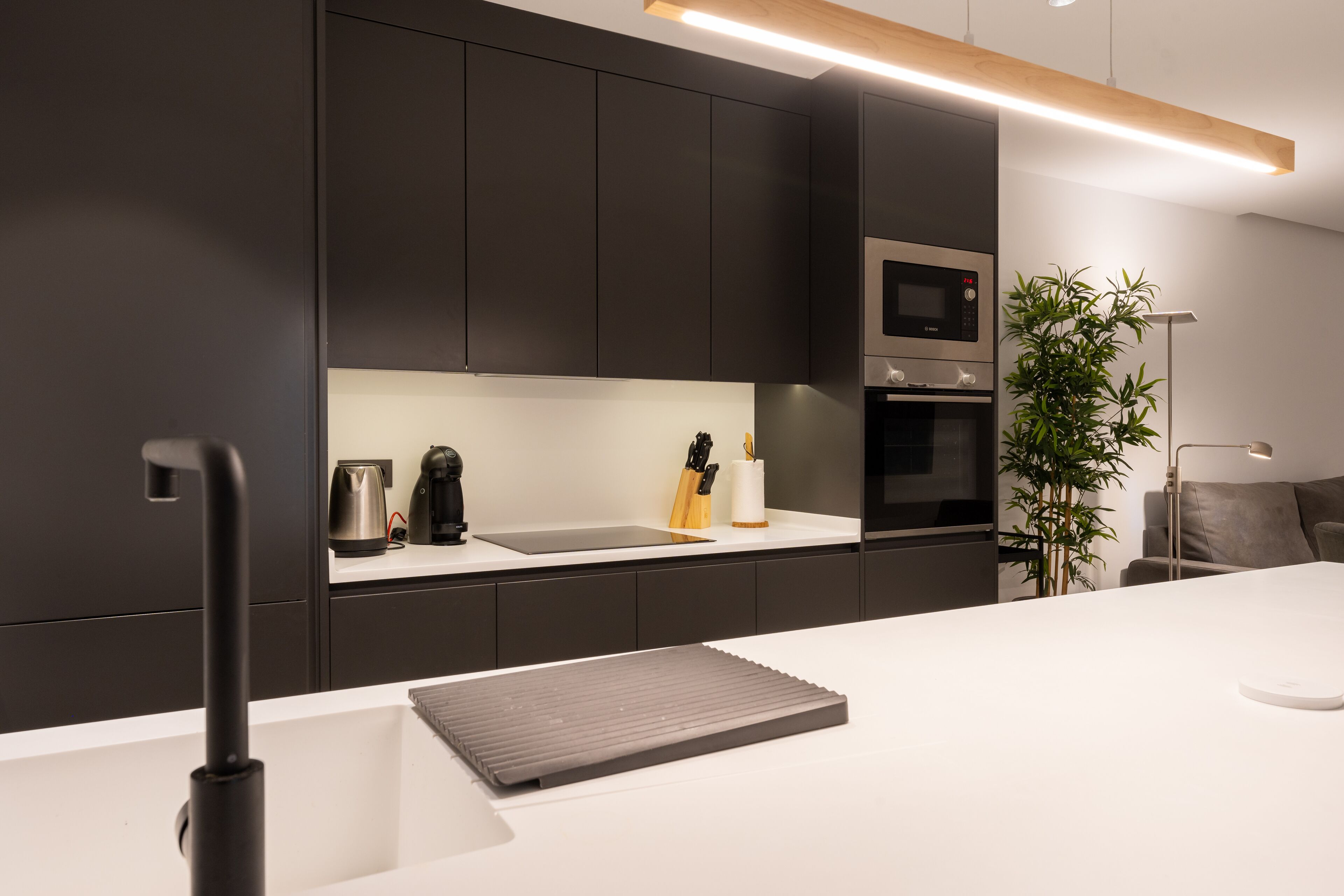 A modern kitchen with dark cabinets, a white countertop, a built-in oven, and a coffee maker.