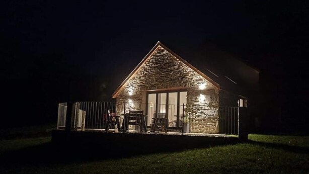 Un edificio de piedra con techo triangular, puerta de cristal y un patio cercado con sillas.