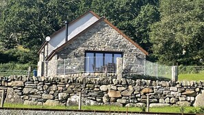 Una casa de piedra con techo inclinado, un pequeño balcón y un muro de piedra al frente.