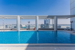 A rooftop pool with clear blue water, surrounded by modern buildings and a clear sky.