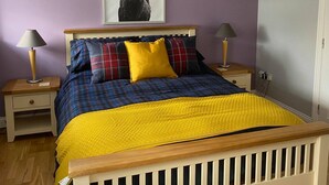 Un dormitorio con una cama, dos mesitas de noche, una lámpara en cada una y un ciervo enmarcado en la pared, además de una puerta a la derecha.
