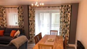 Una sala de estar con sofá, una mesa de comedor con sillas y cortinas estampadas.