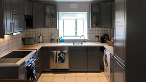 Una cocina moderna con armarios grises, horno empotrado, lavadora y ventana que proporciona luz natural.