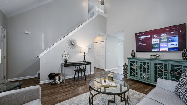 A modern living room with a staircase, a dining area, and a TV displaying various streaming services. - Superb For Traveling Workers Near Cartersville (Cartersville)