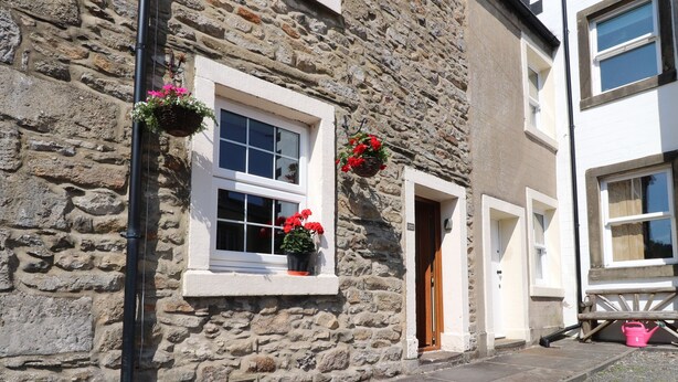 A stone building with a white window and door, a stone wall, and a small step leading to the entrance.