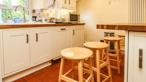 A kitchen with white cabinets, a wooden countertop, a microwave, a coffee maker, and two wooden stools.