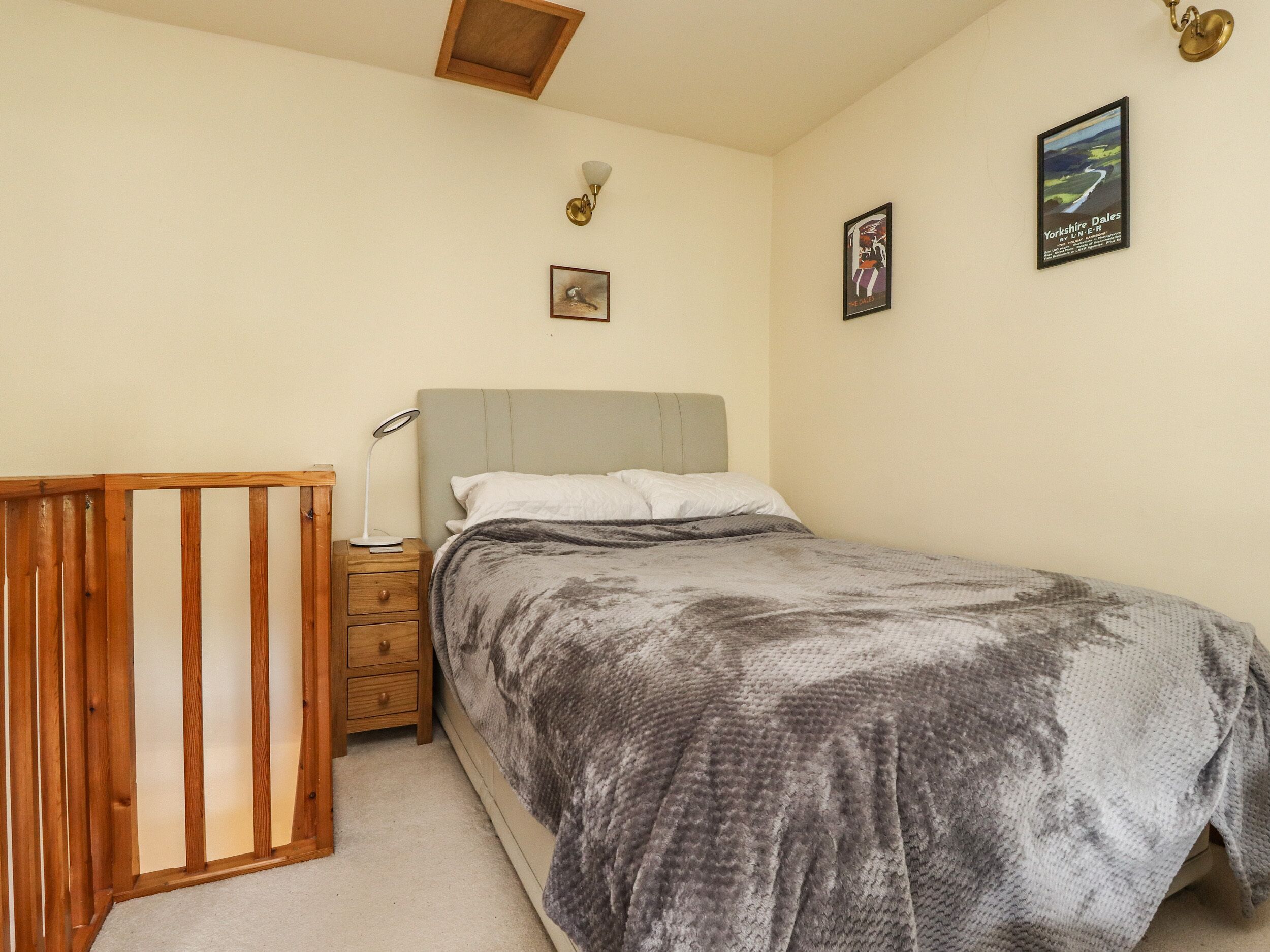 A bedroom with a bed, a nightstand, a lamp, a wooden crib, and two framed pictures on the wall.