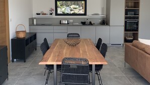 A modern kitchen with a wooden dining table, black chairs, and a television above the counter.