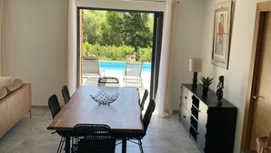 A dining area with a table and chairs, a sofa, a cabinet, and a view of a swimming pool.