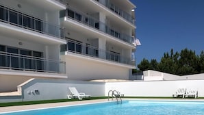 A modern hotel with a rectangular swimming pool, multiple balconies, and white outdoor furniture. - Nazaré Views I - Terrace, Pool & Sea View (Nazaré)