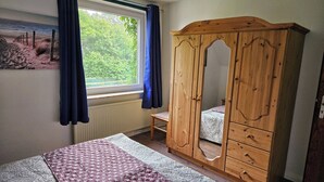Una camera da letto con un letto, un armadio in legno, una finestra con tende e un termosifone.