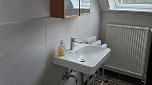 Un bagno moderno con un lucernario, piastrelle bianche, un lavandino bianco e un armadietto da farmacia in legno.