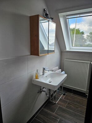 Ein modernes Badezimmer mit Oberlicht, weißen Fliesen, einem weißen Waschbecken und einem Holz-Medizinschrank.