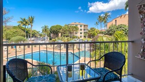 A balcony with a view of a pool, two wicker chairs, and a table with two mugs.
