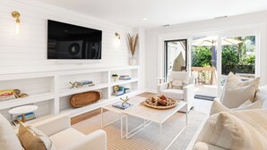 Un moderno salón con una paleta de colores blanco, un televisor de pantalla plana en la pared, una mesa de centro y un sofá.