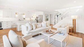Un salón moderno con una decoración en tonos blancos, que incluye un sofá, una mesa de centro y una escalera que sube a un nivel superior.
