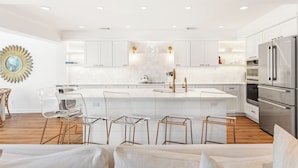 Una cocina moderna con armarios blancos, una isla grande y electrodomésticos de acero inoxidable.