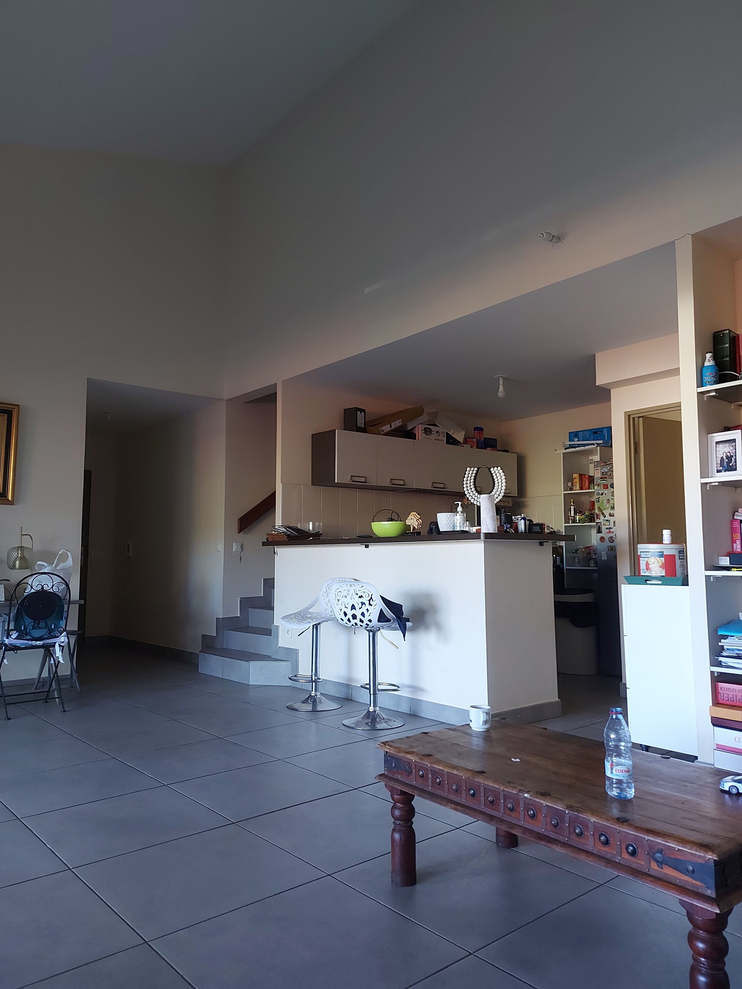 Una sala de estar con una mesa de centro de madera, una silla blanca y una zona de cocina con encimera y armarios.