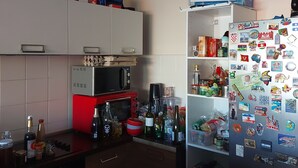 A kitchen with a microwave, stove, and refrigerator. There are various items on the countertops and shelves, including bottles and boxes. - Duplex 160 m2 (Saint Gilles les bains)
