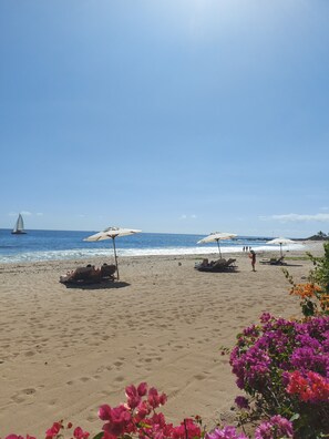 A beach with umbrellas, lounge chairs, and a sailboat in the distance. - Duplex 160 m2 (Saint Gilles les bains)