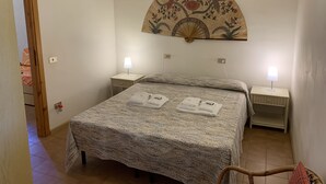 Un dormitorio ordenado con una cama, dos mesitas de noche, un adorno en la pared y una silla.
