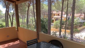 Un balcón con mesa y sillas, con vista a un patio con árboles y edificios.
