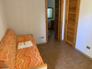 A room with a wooden floor, a sofa with a patterned cover, and a wooden door. - App. 3/4 ps (Santa Margherita di Pula)