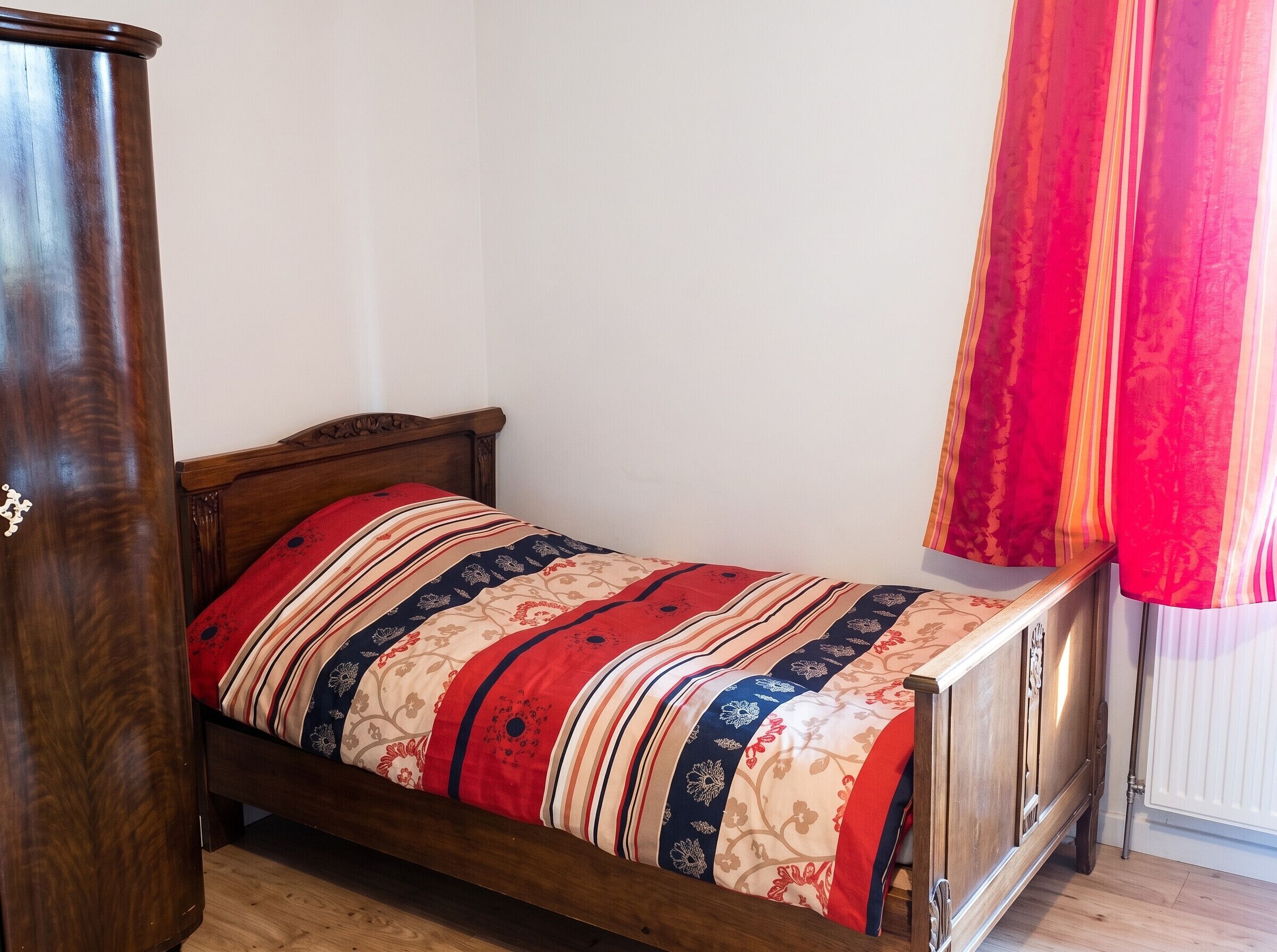 Ein Einzelbett mit einem gemusterten Bettdecken, einem hölzernen Kopfteil und einem Holzschrank.