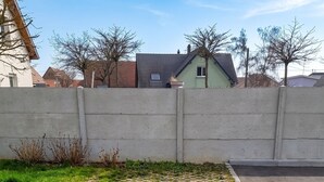 A paved area with hexagonal tiles and grass patches, bordered by a concrete wall and a road. - Homerez - House in Berrwiller (Berrwiller)