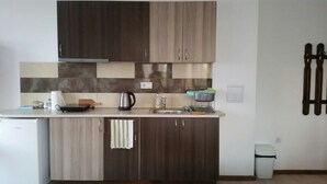A compact kitchen with dark wood cabinets, a stainless steel range hood, a kettle, a sink, and a trash bin. - Inviting 1-bed Apartment in Aleksandrovo (Pomorie)