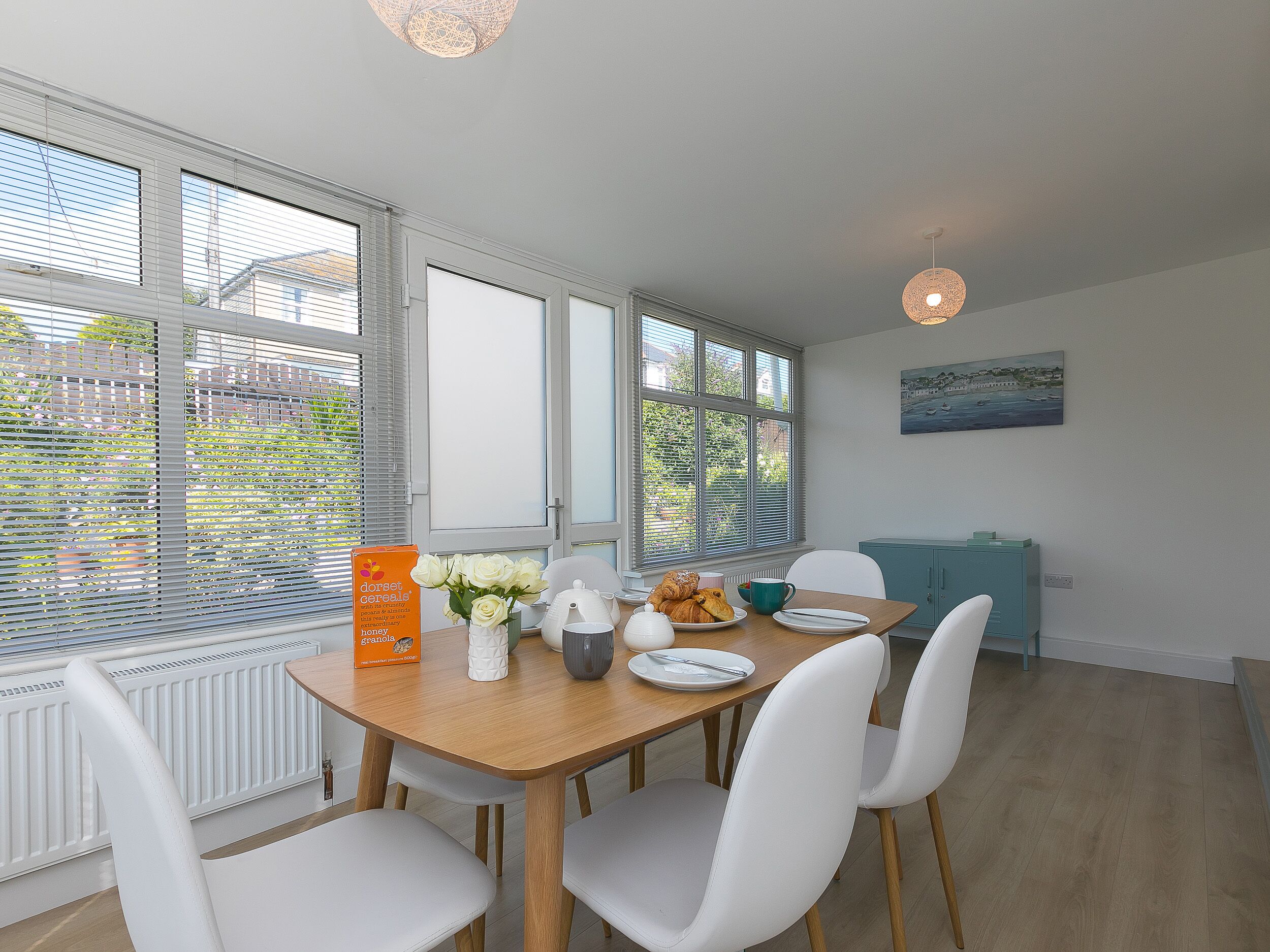 A dining area with a wooden table, white chairs, a vase of flowers, and a breakfast setting.