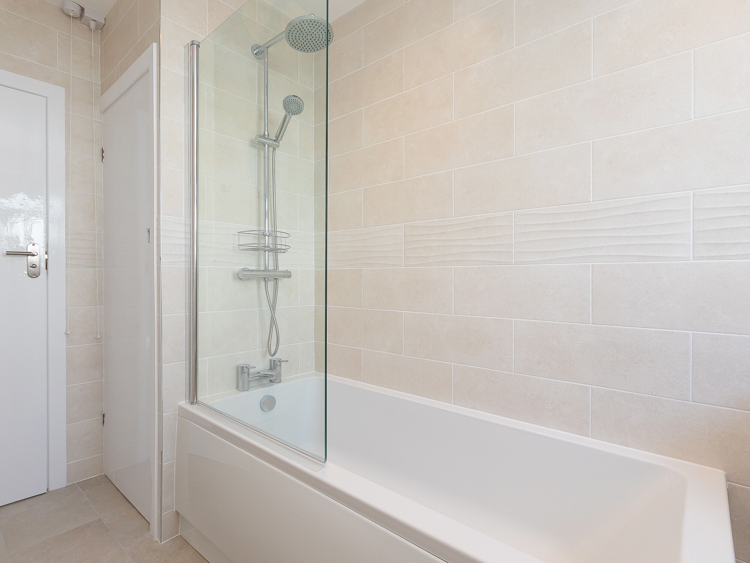 Een moderne badkamer met een glazen douchecabine, een wit bad en beigekleurige betegelde wanden.