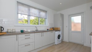 Une cuisine moderne avec des meubles blancs, un lave-linge encastré et une fenêtre donnant sur un espace verdoyant.
