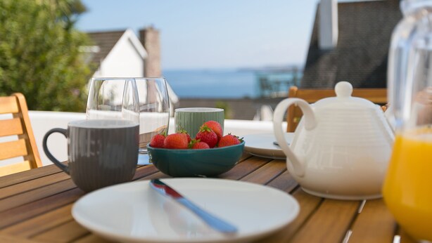 Une table de petit-déjeuner avec un bol de fraises, une tasse de café, une théière et un verre de jus d’orange.