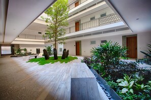 A spacious indoor atrium with a central tree, multiple balconies, and a variety of indoor plants.