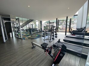 Et moderne fitnesscenter med løbebånd, styrketræningsudstyr og et stort vindue med udsigt over byen.