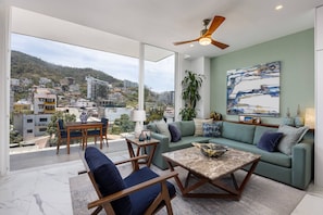 A modern living room with a large window, a ceiling fan, and a view of a hillside.