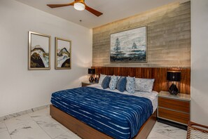 A bedroom with a bed, headboard, nightstands, lamps, and artwork.