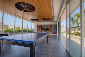 A spacious room with a ping pong table, large windows, and a ceiling fan.