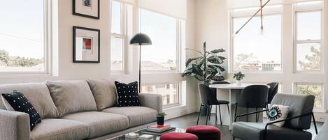 A modern living room with a sofa, coffee table, ottomans, and a dining area with chairs and a table.