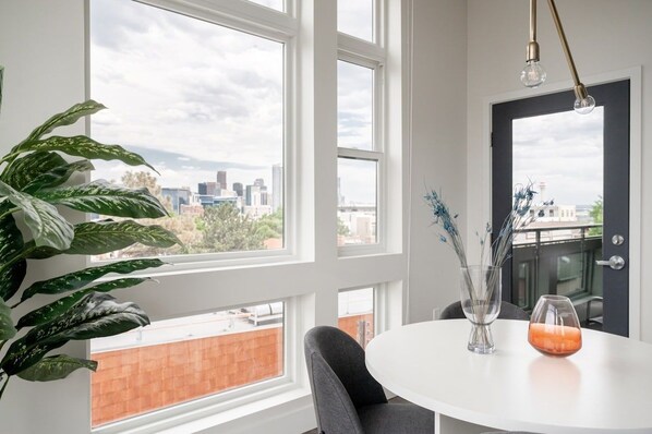 A room with large windows, a round table, a potted plant, and a vase with flowers.