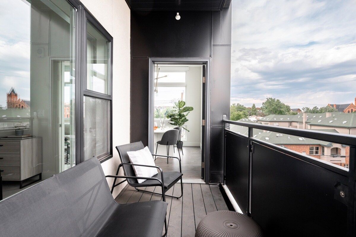 A balcony with a view of a cityscape, a seating area with chairs, and a potted plant.