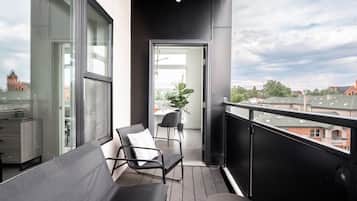 A balcony with a view of a cityscape, a seating area with chairs, and a potted plant.