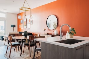 A modern kitchen with a central island, dining area, and a large window.