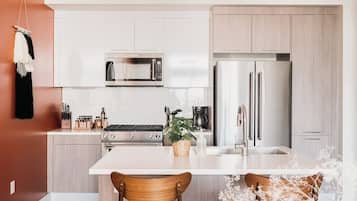 Een moderne keuken met witte kasten, een roestvrijstalen koelkast, een magnetron en een gasfornuis.