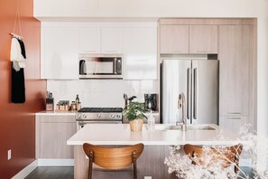 A modern kitchen with white cabinetry, a stainless steel refrigerator, a microwave, and a gas stove. - Gallery Retreat | Skyline Views | Zuni Lofts (Denver)