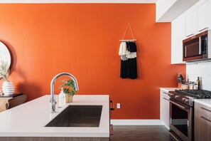 Eine Küche mit weißer Arbeitsplatte, Edelstahlgeräten und einer orangefarbenen Wand.