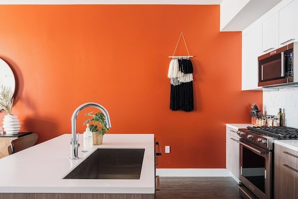 A kitchen with a white countertop, stainless steel appliances, and an orange wall.